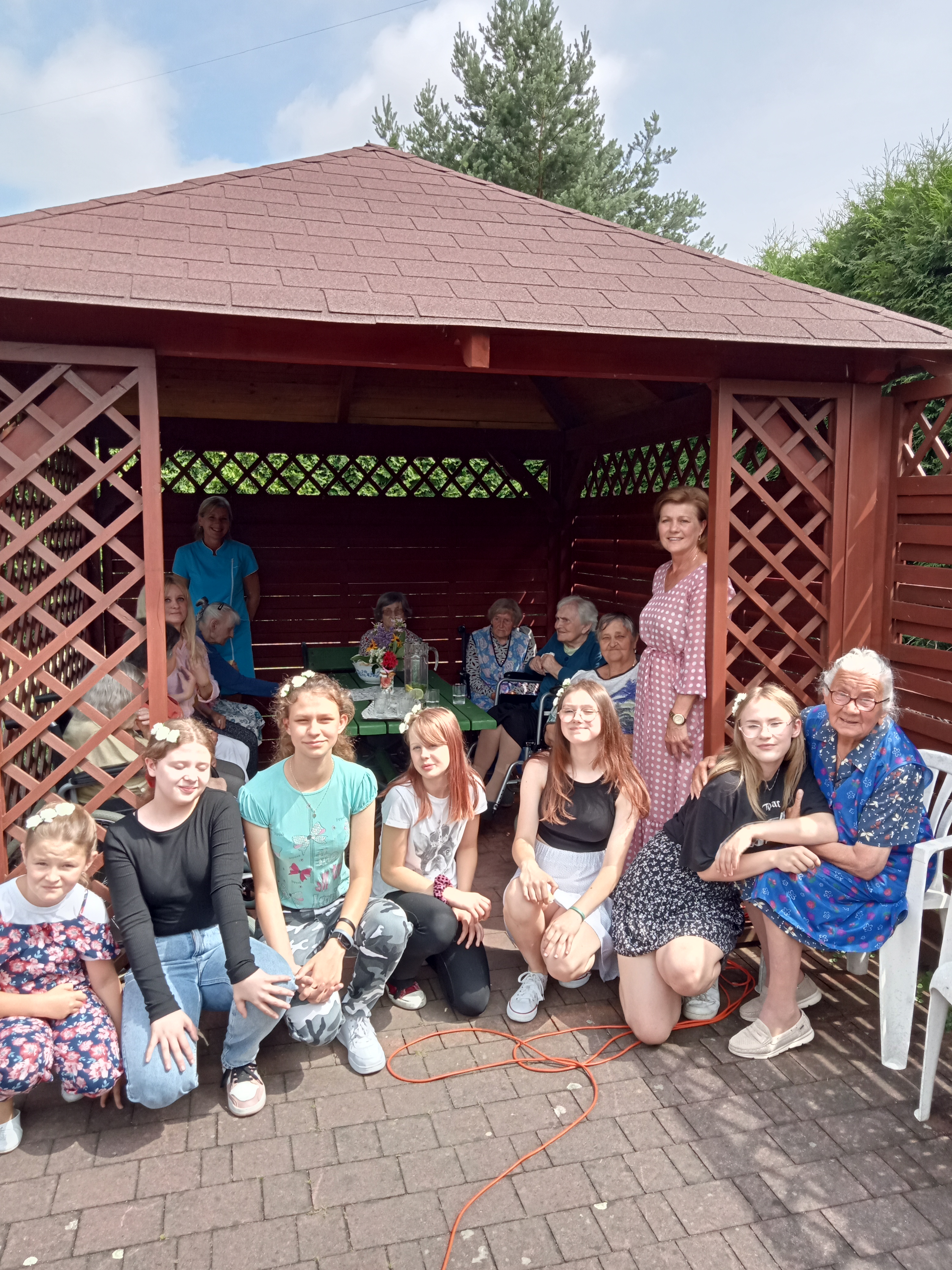 Mieszkanki DPS wsp&oacute;lnie z dziewczynkami, opiekunami na tle altany ogrodowej